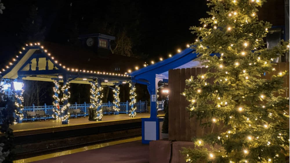 Festive train station at night adorned with twinkling lights and holiday decorations.