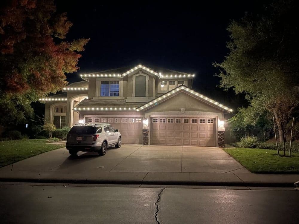 Modern home illuminated by decorative lights at night, with a parked SUV in the driveway.